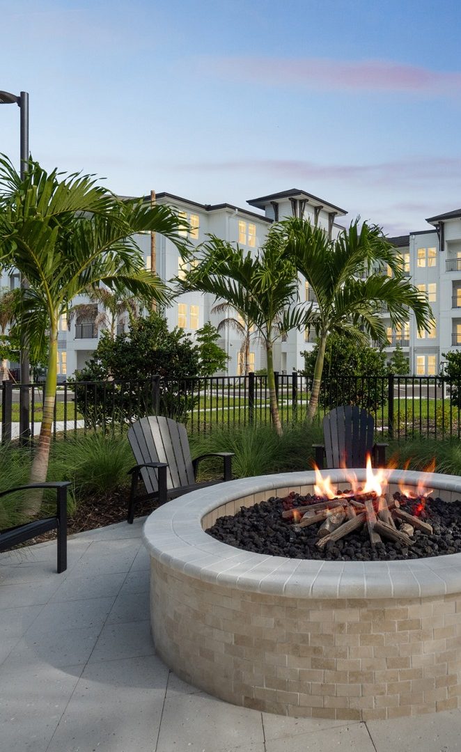 Fire pit at dusk with building exterior of Alton Osprey apartment homes